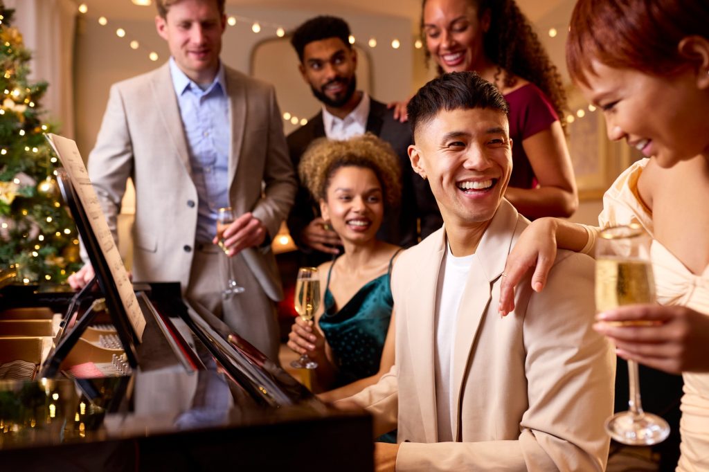 Group Of Friends Around Piano Celebrating At Christmas Or New Year Party Together